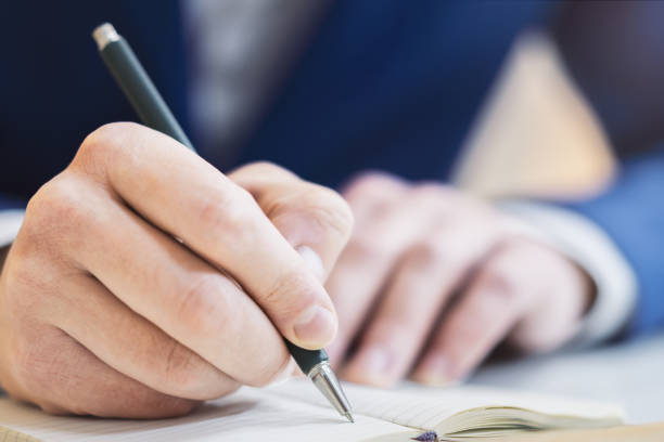 istock A man's hand seen in close-up, writing in a notepad, against a soft-focus backdrop 1498083513