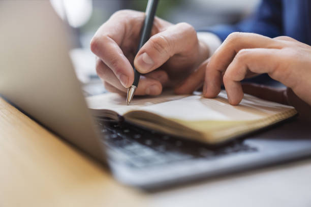 istock A man's hand seen in close-up, writing in a notepad on a contemporary laptop, against a soft-focus backdrop 1498083530