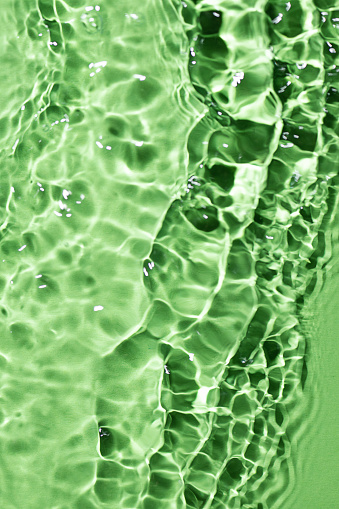 Light green water surface texture with splashes and bubbles. Abstract background for natural beauty products. Green water splashes wallpaper.