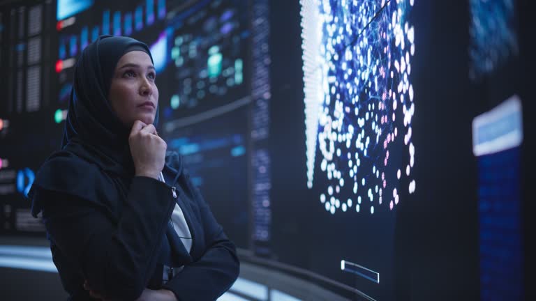 Portrait of a Smart Focused Middle Eastern Software Engineer Analyzing Neural Network Big Data on a Digital Screen. Young Arab Woman in Hijab Working in an Innovative Internet Service Company