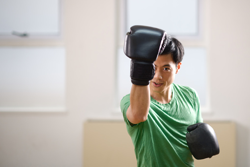 Asian male athlete portrait boxing gloves in focus upper cut in a boxing gym in Cape Town, South Africa