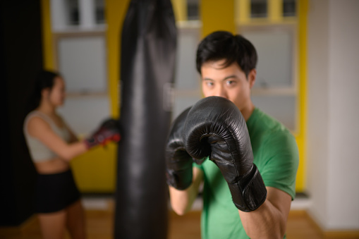 Asian male shadow boxing in a gym with female Chinese boxer punching punchbag in a boxing gym in Cape Town, South Africa.