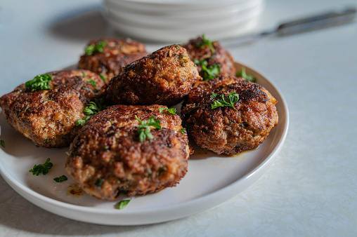 Homemade fresh pan fried german pork meatballs or frikadellen. Served ready to eat on a plate or platter with chopped parsley. Closeup, front view