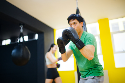 Asian male shadow boxing in a gym with female Chinese boxer punching punchbag in a boxing gym in Cape Town, South Africa.