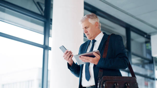 viaggiatore, tablet e smartphone uomo d'affari con software multimediale per la produttività, l'e-commerce e il networking in movimento. senior manager aziendale che cammina con la tecnologia per controllare l'aggiornamento dell'interfaccia utente ux - business ceo building activity business person foto e immagini stock