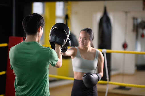 Well lit Female and Male Chinese Athletes Hook and Jab punches in boxing ring boxing practise in a gym in Cape Town, South Africa.  Hook and Jab pads and boxing gloves are being worn.