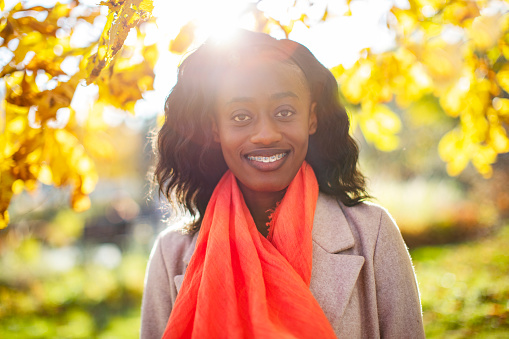 Young adult black woman portrait in red scarf at sunny weather in park