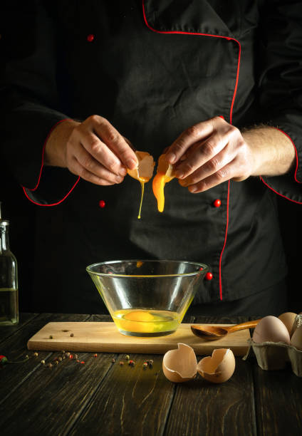 istock The cook pours a raw egg into a bowl. Delicious breakfast menu idea for hotel or restaurant on black background 1498098819