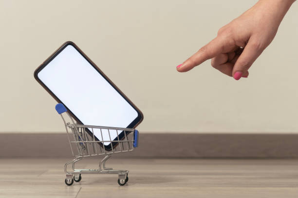 Ecommerce concept image: woman pointing a cart with a blank screen smartphone inside