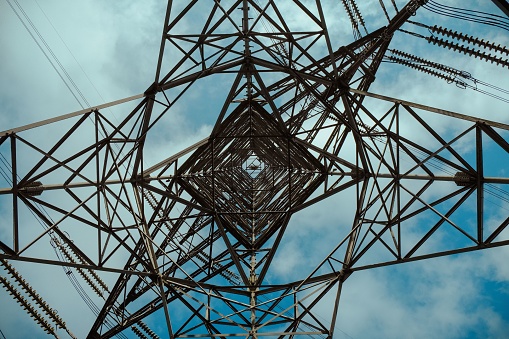 A close-up of an electricity pylon illuminated by a bright sun in the background