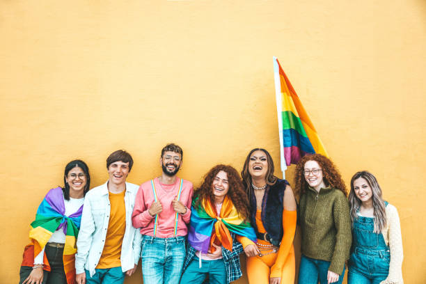 Diverse group of young people celebrating gay pride festival day - Lgbt community concept with guys and girls hugging together outdoors - Multiracial cheerful friends standing on a yellow background stock photo