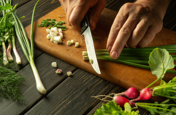 The chef cuts the onion with a knife on the kitchen cutting board. Vegetarian products or fresh vegetables on the kitchen table for a healthy lunch