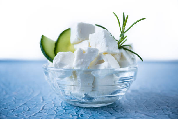 Feta cheese, cucumber and herbs in a bowl on blue background