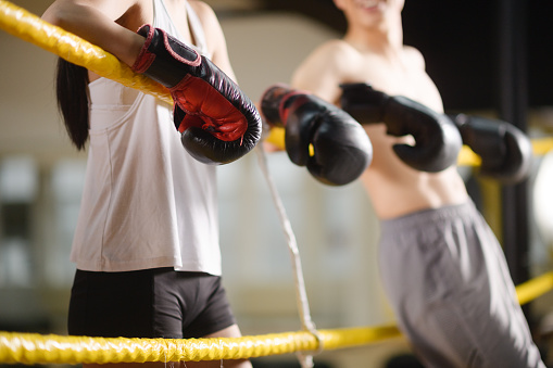 Mid section Female and Shirtless Male Boxers taking a break standing with boxing gloves focus in a gym in Cape Town, South Africa.