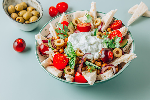 Healhty vegetarian salad with fried chickpeas, pita, olives, fresh vegetables and tzatziki sauce over green background. Clean healthy eating concept. Selective focus