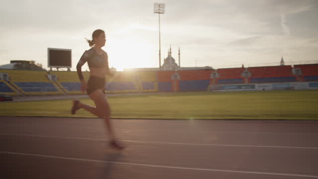Fit female sprinter running fast in stadium during morning training