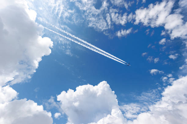Airliner with Contrails Flying in a Blue Sky with Beautiful Cumulus Clouds stock photo