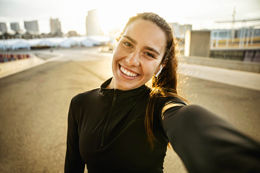 Sportswoman female athlete smile holding a mobile phone - Happy runner girl taking selfie picture on city street - Social media and sport life style concept