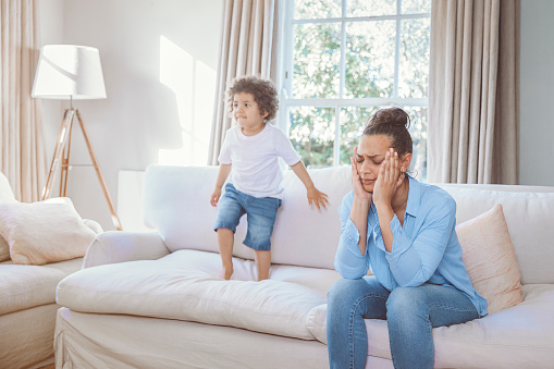 Exhausted mother sitting on the couch while her kid running at home