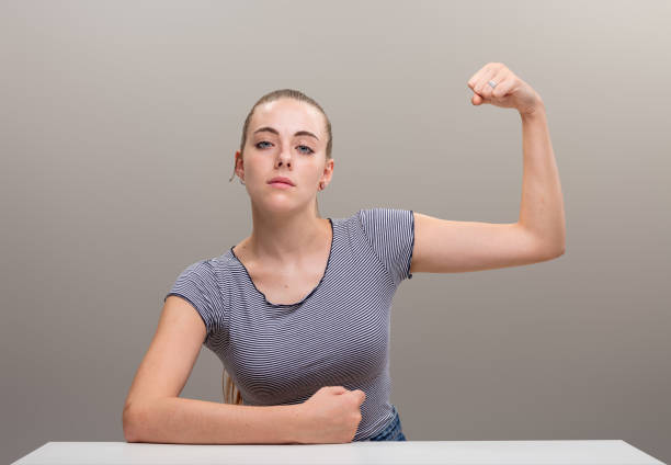 Strong young woman leans on her forearm in a manly way and flexes her other muscle, pulling it with her fist. Her cocky and confident expression says she won't be ordered around, she's her own boss