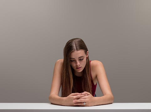 A beautiful girl with long hair, broad lean shoulders, nervously wrings her hands on a table. Her gaze is downcast, sad, because everyone has their own way of suffering, pain is subjective, and she se