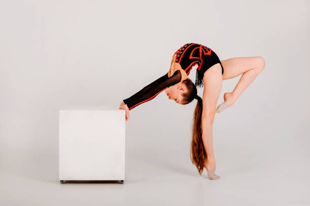 A girl gymnast in a black leotard does tricks on a white cube on a white background stock photo
