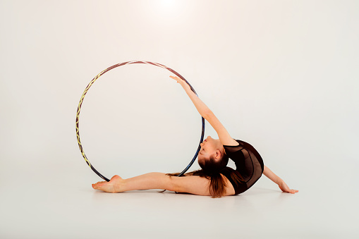 A girl gymnast in a black leotard with a with hoop on a white background. Rhythmic gymnastics concept. Front view