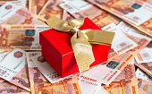 A gift with a gold satin ribbon lying on Russian banknotes. The concept of finance, investment, savings and cash.