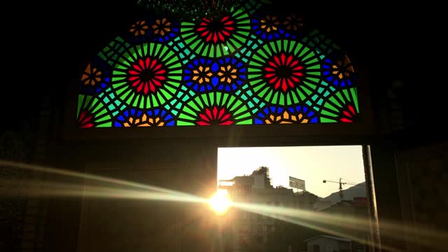 Sun shines behind the door of a mosque while  people in silhouette exit out from it