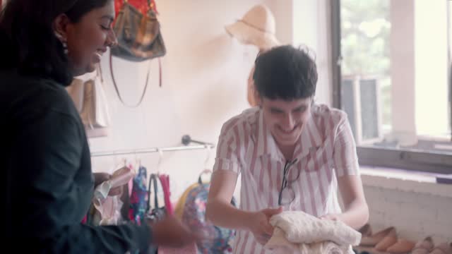 Middle Eastern Gender Fluid Person and Indian Woman Sorting Folding Clothes for Donation