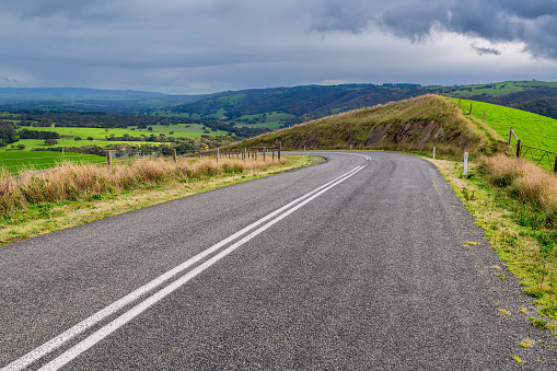 Plain asphalt road turning right through Adelaide Hills farms during winter season, South Australia