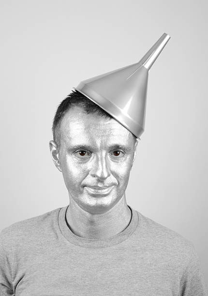 Mid adult man wearing silver make up, silver funnel as a hat and grey t-shit on light grey background as OZ wizard's Tin Man