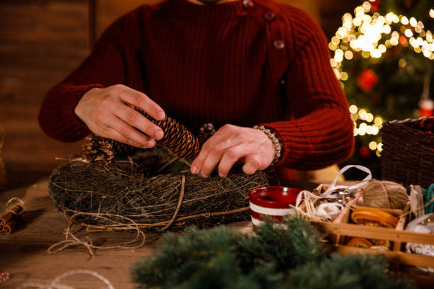 istock Creative young man decorating a Christmas wreath with pine cones and ornaments 1498116867