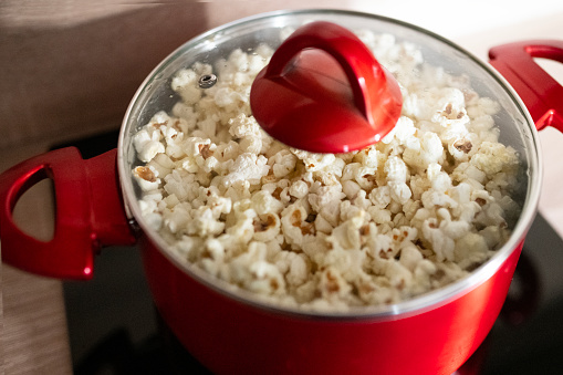 Home made popcorn  in a red pot , \npopular snack in the cinema.