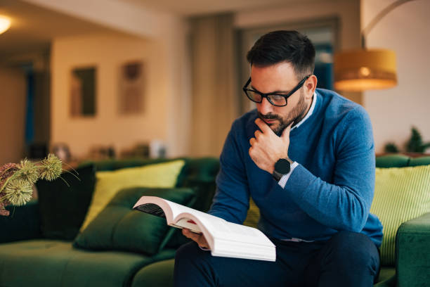 istock Focused businessman reading a book, sitting on the couch. 1498119720