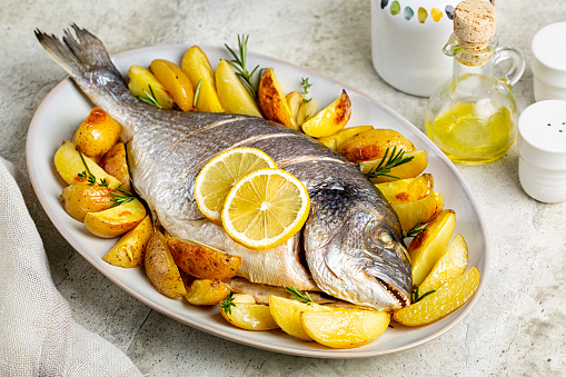 Meal with baked sea bream or dorada fish with baked potato, lemon and herbs.