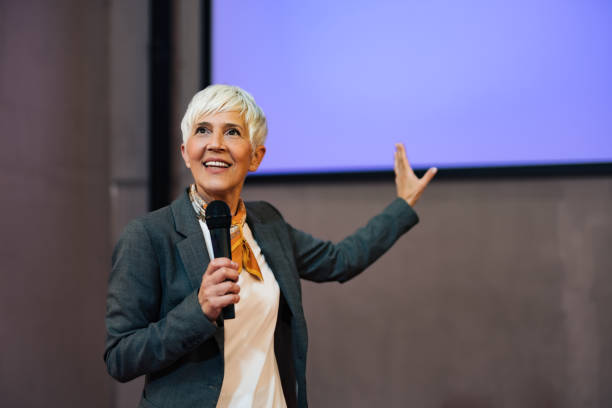 istock A smiling woman giving a speech, pointing at the projection screen, elegantly dressed. 1498120359