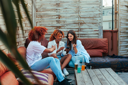 Three diverse young people relaxing on the rooftop and using the phone