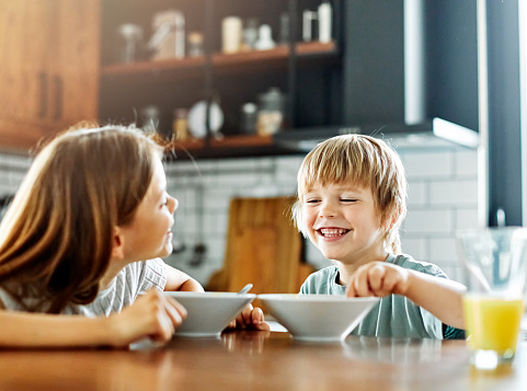 Portrait of brother and sister having fun together eating breakfast in kitchen