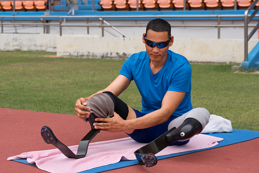 portrait of an Asian paragame athlete, seated on a stadium track, busily affixing his running blades, preparing for intense training