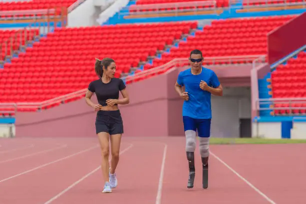 A para game speed runner with prosthetic running blades, alongside his female trainer, warms up with a jog on the running track before practice