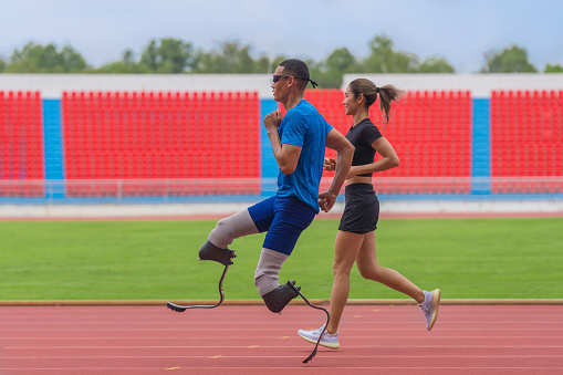 A male speed runner with two prosthetic blades is seen warming up on the track with his female trainer, preparing to practice