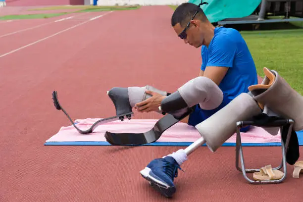 portrait of an Asian paralympic athlete, seated on a stadium track, busily affixing his running blades, preparing for intense training