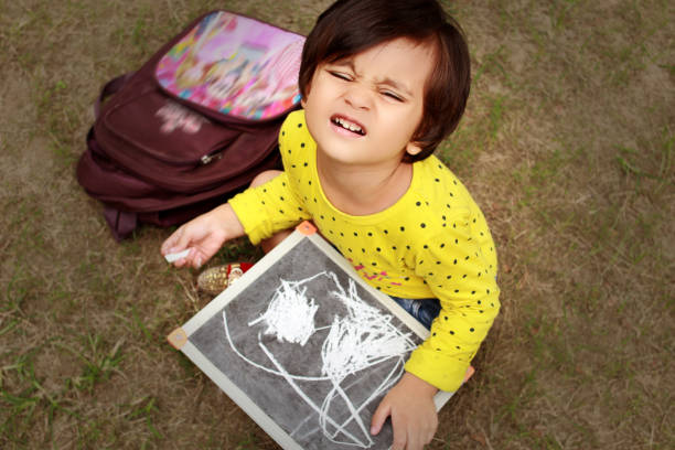 Small baby girl writing on writing slate outdoors in the park.