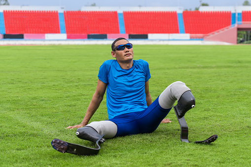 Asian paralympic athlete, poised on the grass lawn with his prosthetic running blades, patiently awaits to start his running practice at the sports stadium
