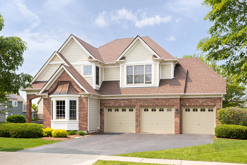 Naperville, IL, USA - May 17, 2023: A large home with a red brick and yellow siding, three car garage, and beautiful landscaping.