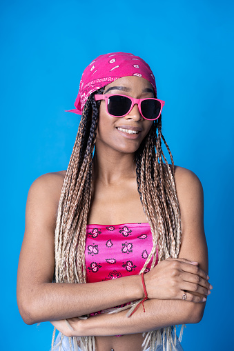 Cool looking woman smiling at the camera, wearing sunglasses and pink bandana against blue background