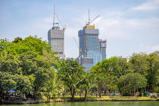 Lumphini Park, Bangkok, Thailand - March 25th 2023: View to the skyline of the still expanding modern Bangkok over a lake in the large public park in the center of the capital of Thailand