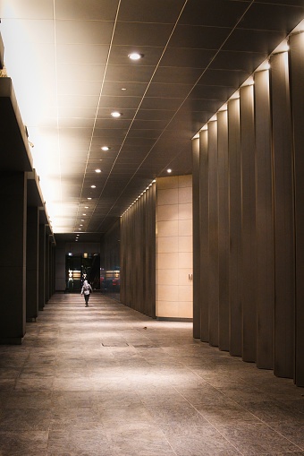 A woman is walking through a long hallway with two empty elevators