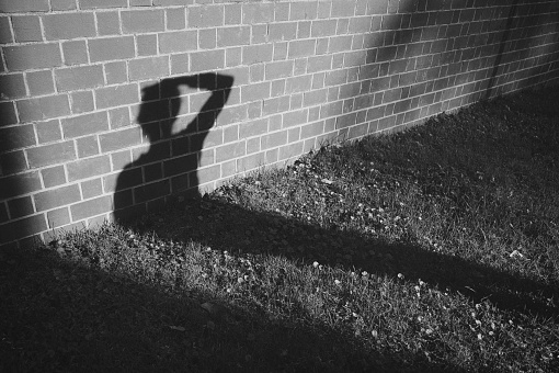 The silhouette of a human figure stands out against a brick wall backdrop, illuminated by a light source to the side which casts a shadow